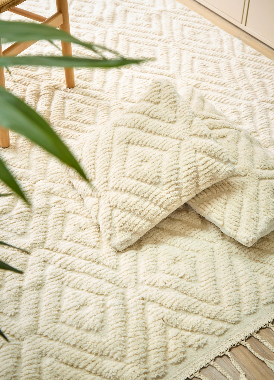 A natural wool cream berber rug with a diamond design and matching cushions on a wooden floor next to a plant