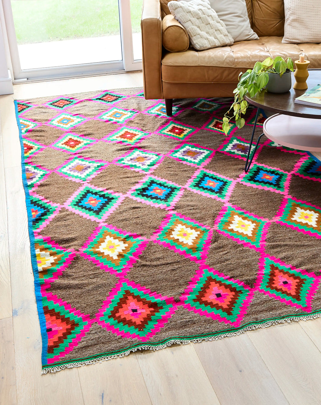 Multicoloured diamond berber rug with leather sofa and table on top next to window