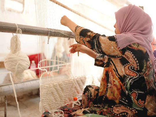 A berber weaver making a natural wool cream berber rug by hand using a traditional loom.