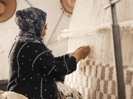 A berber artisan weaving a checkered berber rug with natural wool on a traditional machine 