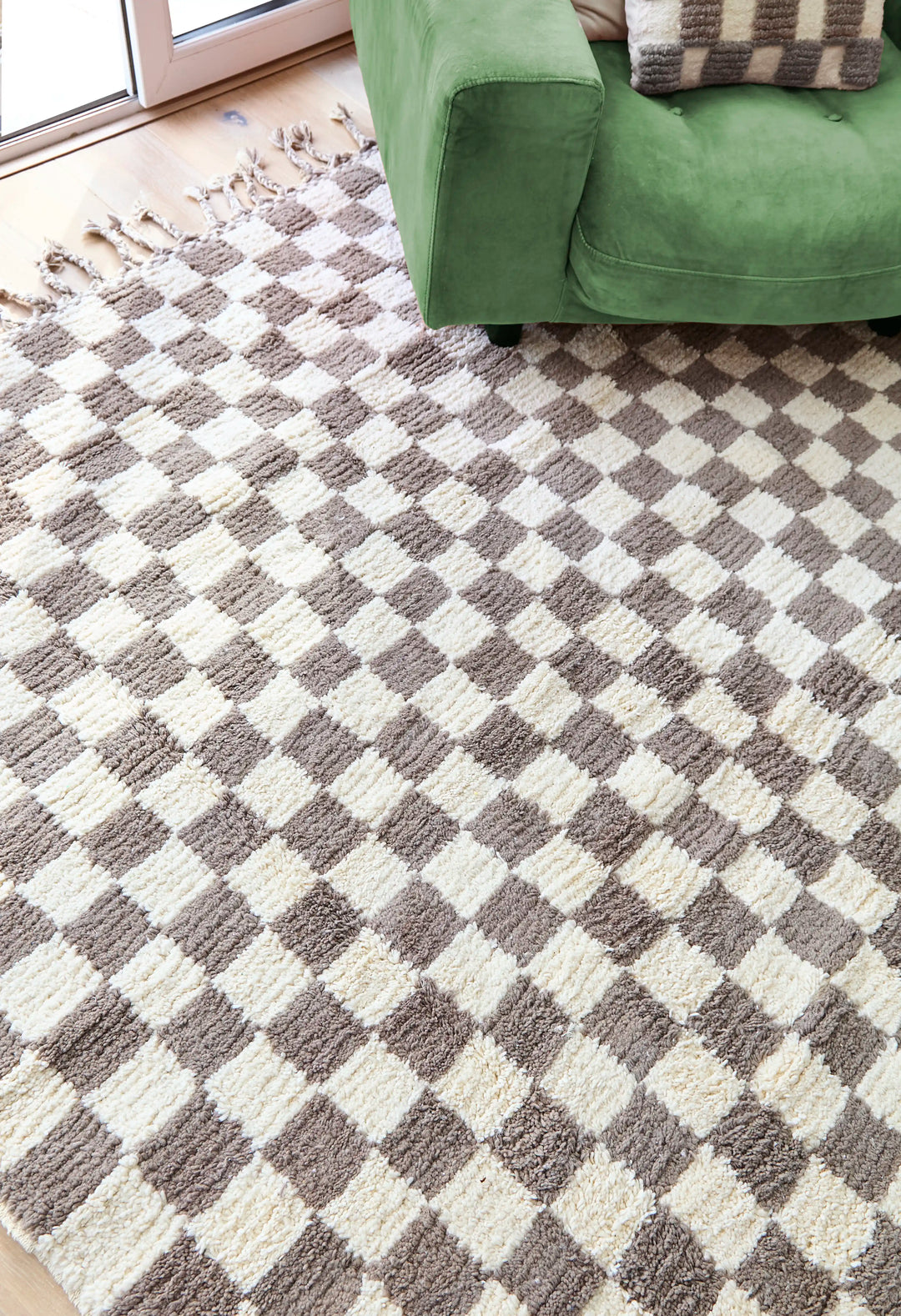 A checkered wool berber rug in taupe and cream on a wooden floor with a green armchair on top