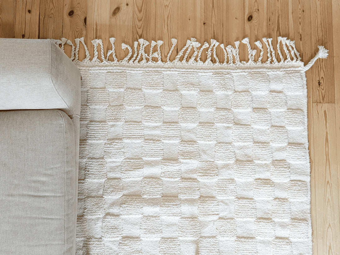 A checkered ivory wool berber rug with cotton plaited tassels on a wooden floor 