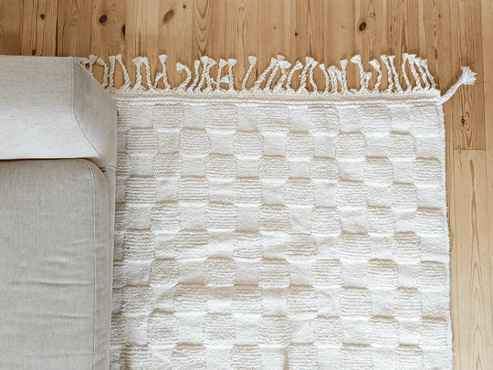 A checkered ivory wool berber rug with cotton plaited tassels on a wooden floor 
