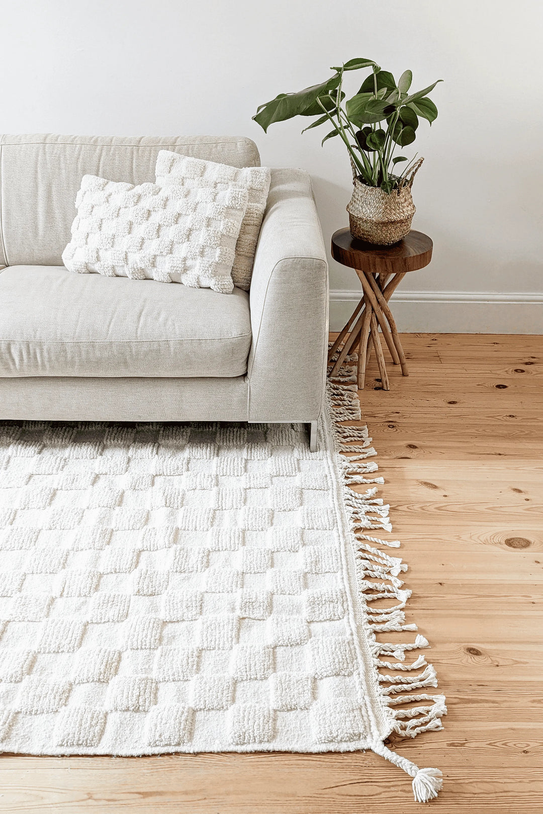 A white checkered berber rug and cushions next to a cream sofa and table with a plant