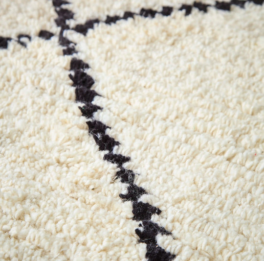 A close up of a cream wool berber rug with black diamond pattern