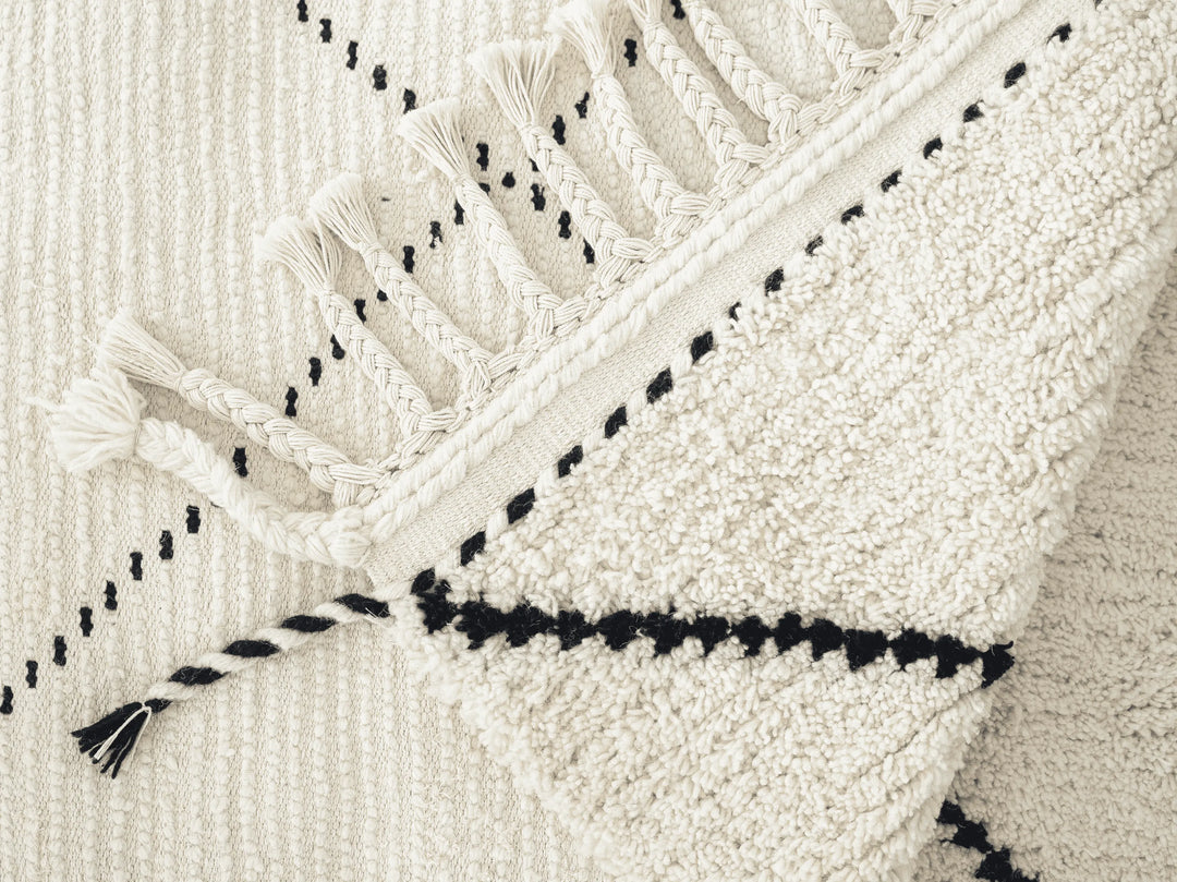 A cream wool berber rug with a black diamond pattern and plaited tassels folded over.