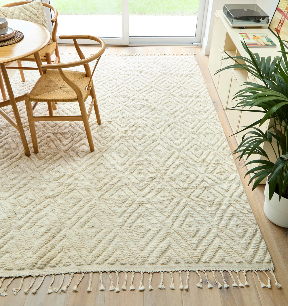 A natural wool cream berber rug with a diamond design on a wooden floor next to a patio door with a wooden table on top.