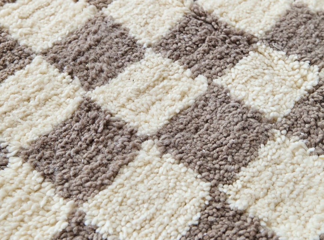 A close up of a checkered taupe and cream berber rug showing the natural wool fibres