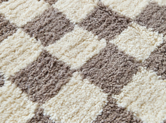 A close up of a checkered taupe and cream berber rug showing the natural wool fibres