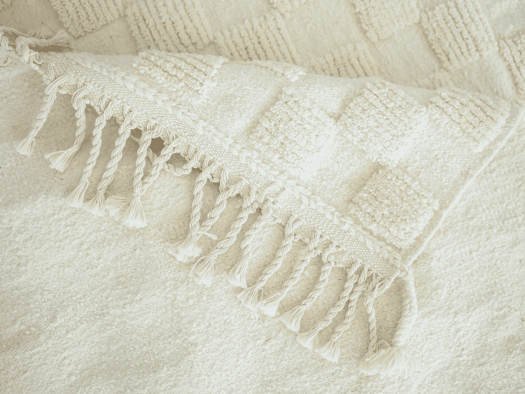A checkered ivory wool berber rug with cotton plaited tassels folded over