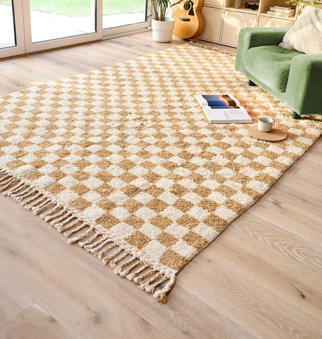 A checkered ochre berber rug with a green armchair and open book on top, in a sunlit room.