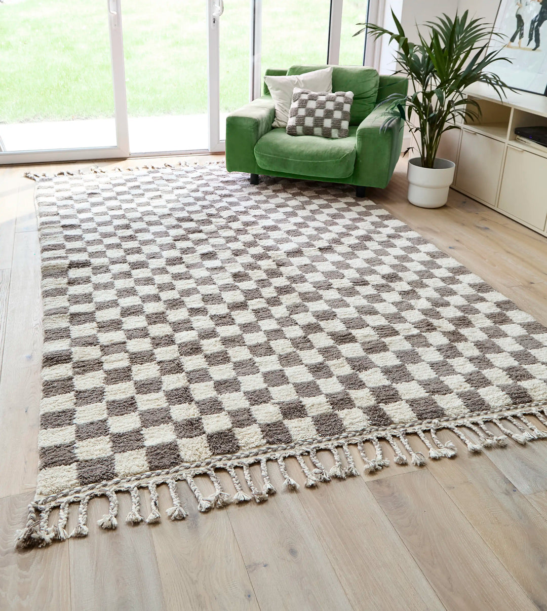 A checkered wool berber rug in taupe and cream on a wooden floor, next to a green sofa and open patio doors.