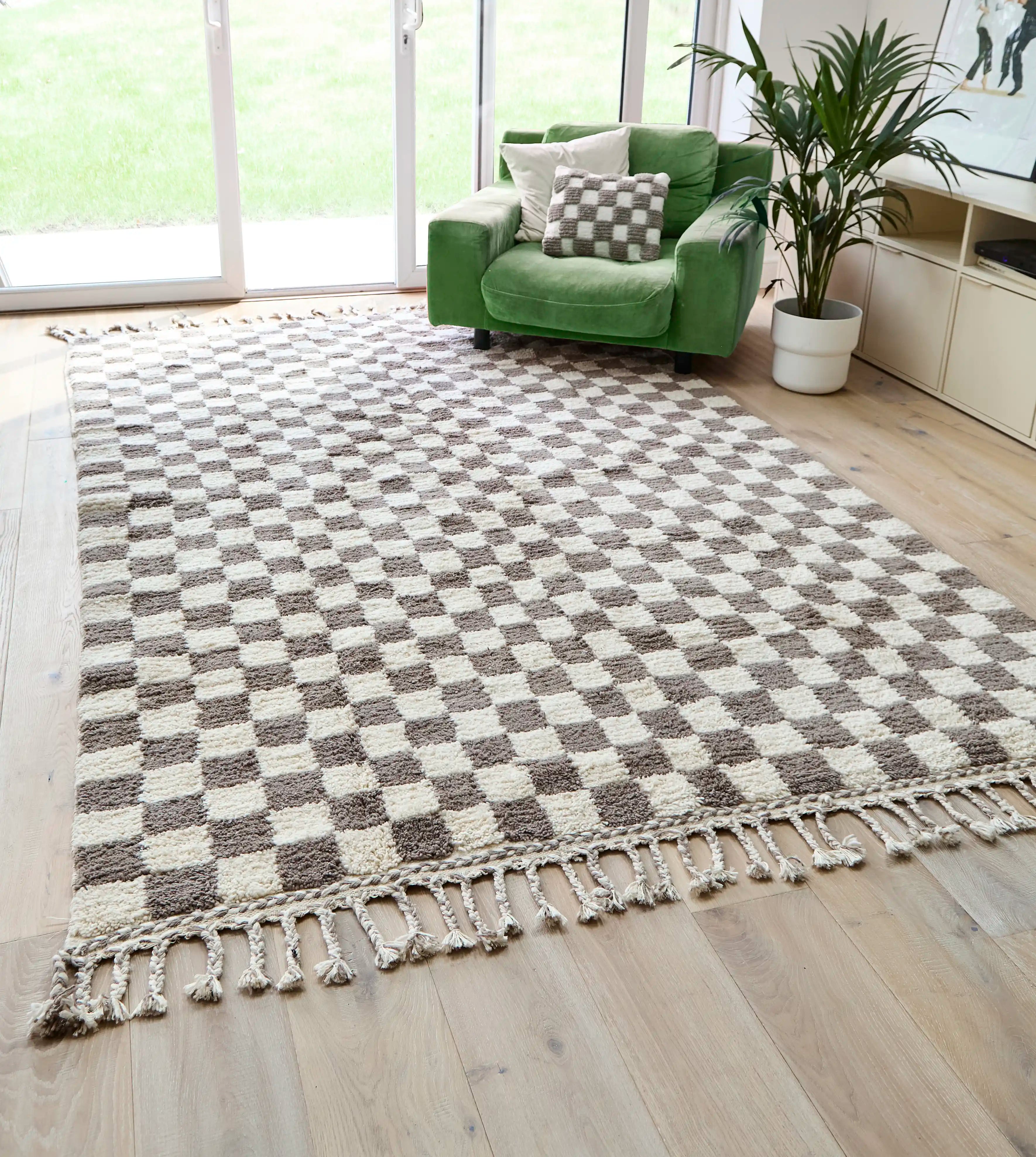 A checkered wool berber rug in taupe and cream on a wooden floor, next to a green sofa and open patio doors.