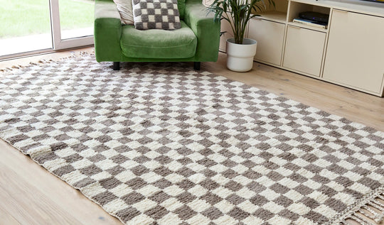 A checkered wool berber rug in taupe and cream on a wooden floor next to a green armchair and open patio doors