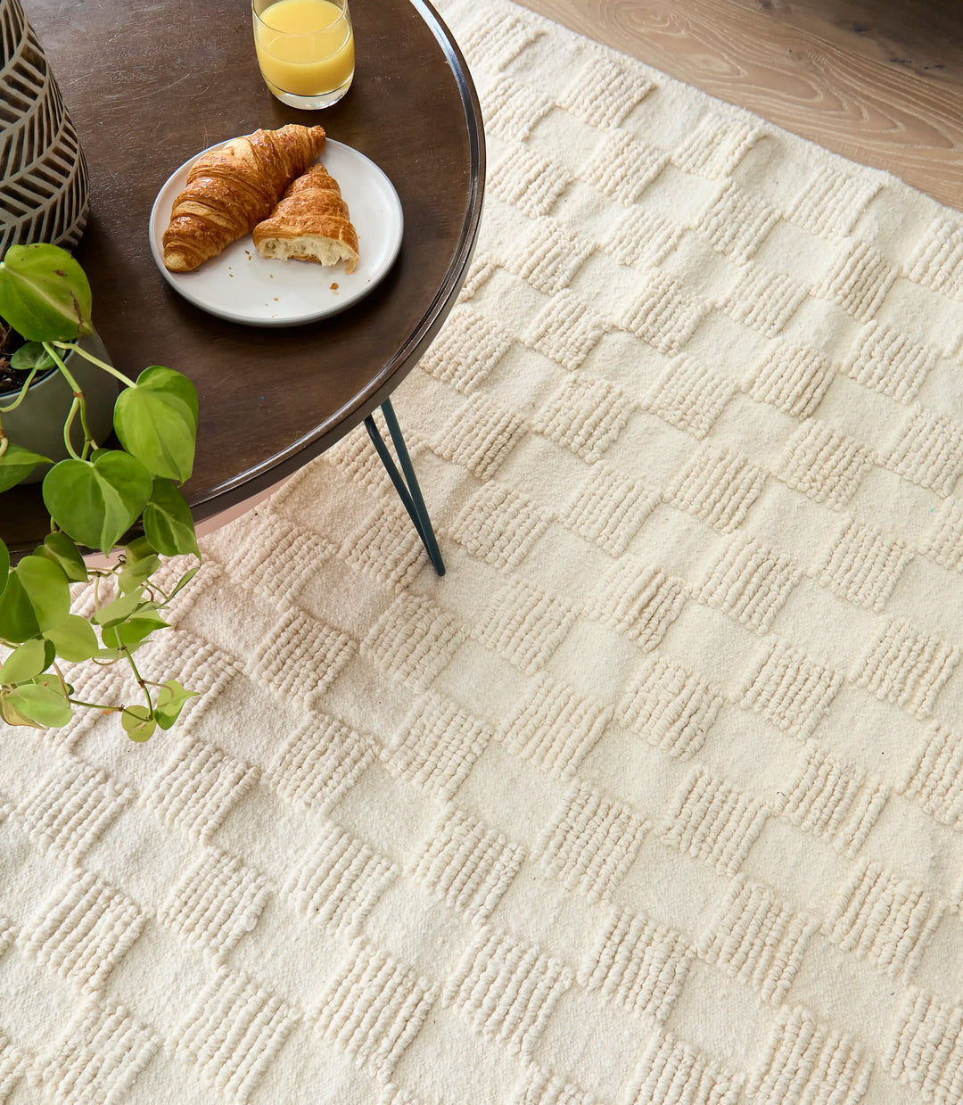 ​Handwoven cream Berber rug with square geometric design shot from above. A table with a croissant and orange juice sits on it.