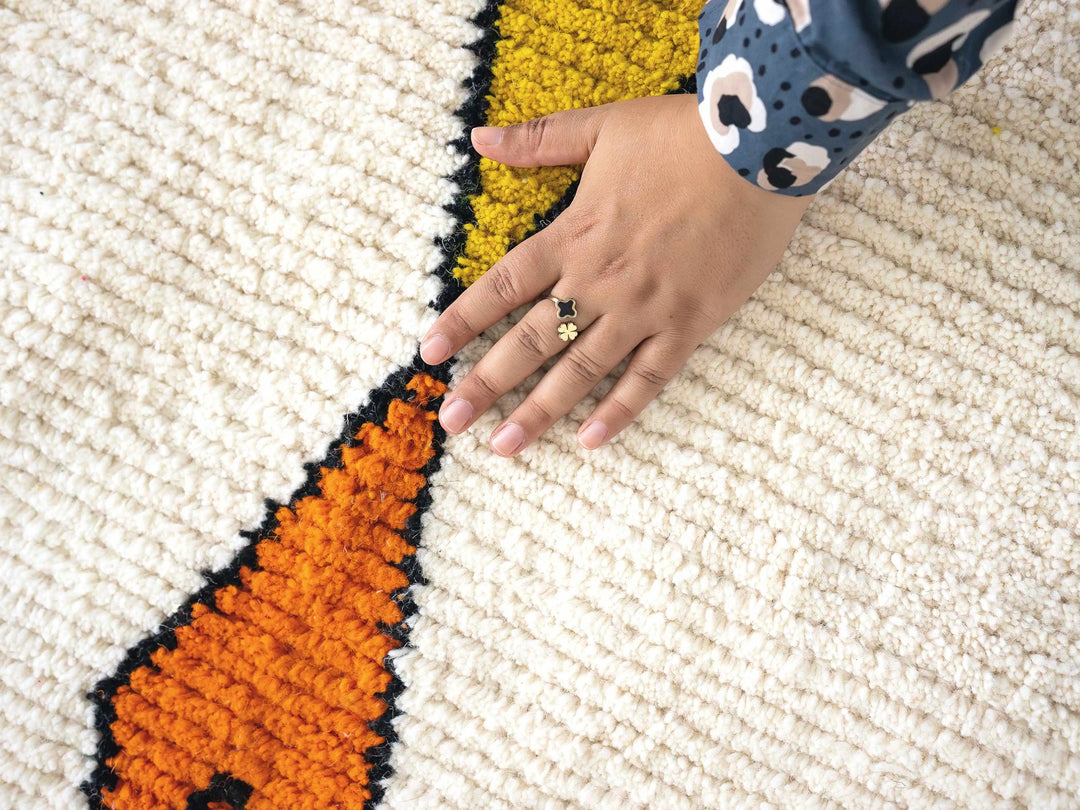 Close up of hand with ring on handmade Berber rug with orange and yellow diamond motif
