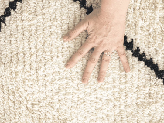 Hand wearing a heart ring strokes the wool on a cream berber rug with diamond pattern