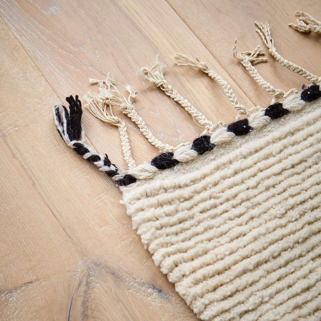 Plaited tassels and a black and white edge on a wool berber rug on a wooden floor