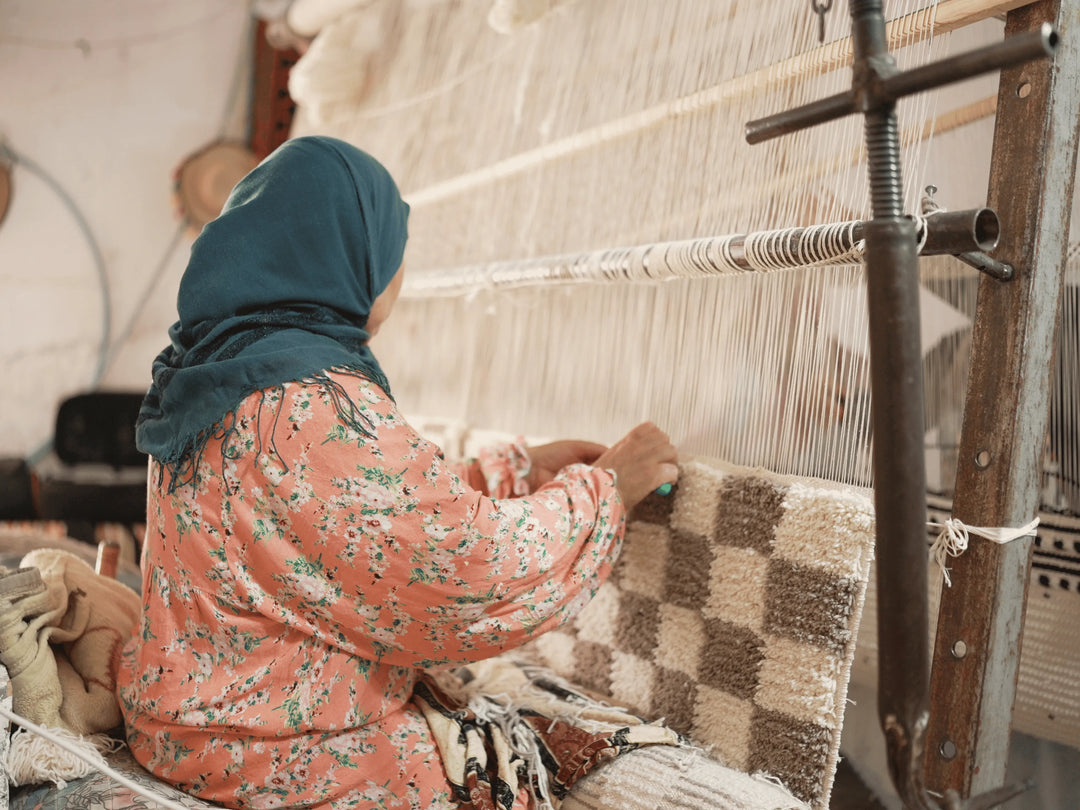 A berber arisan handmaking a wool rug with a checkered design on a traditional machine.