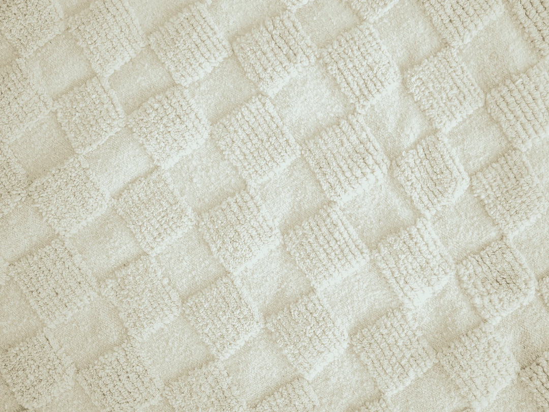 A close up of a natural wool berber rug with repeating ivory geometric squares