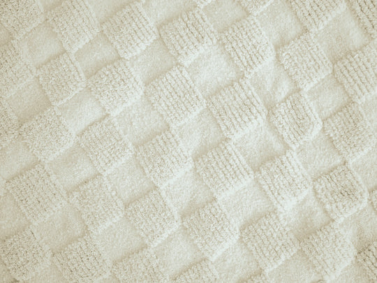 A close up of a natural wool berber rug with repeating ivory geometric squares