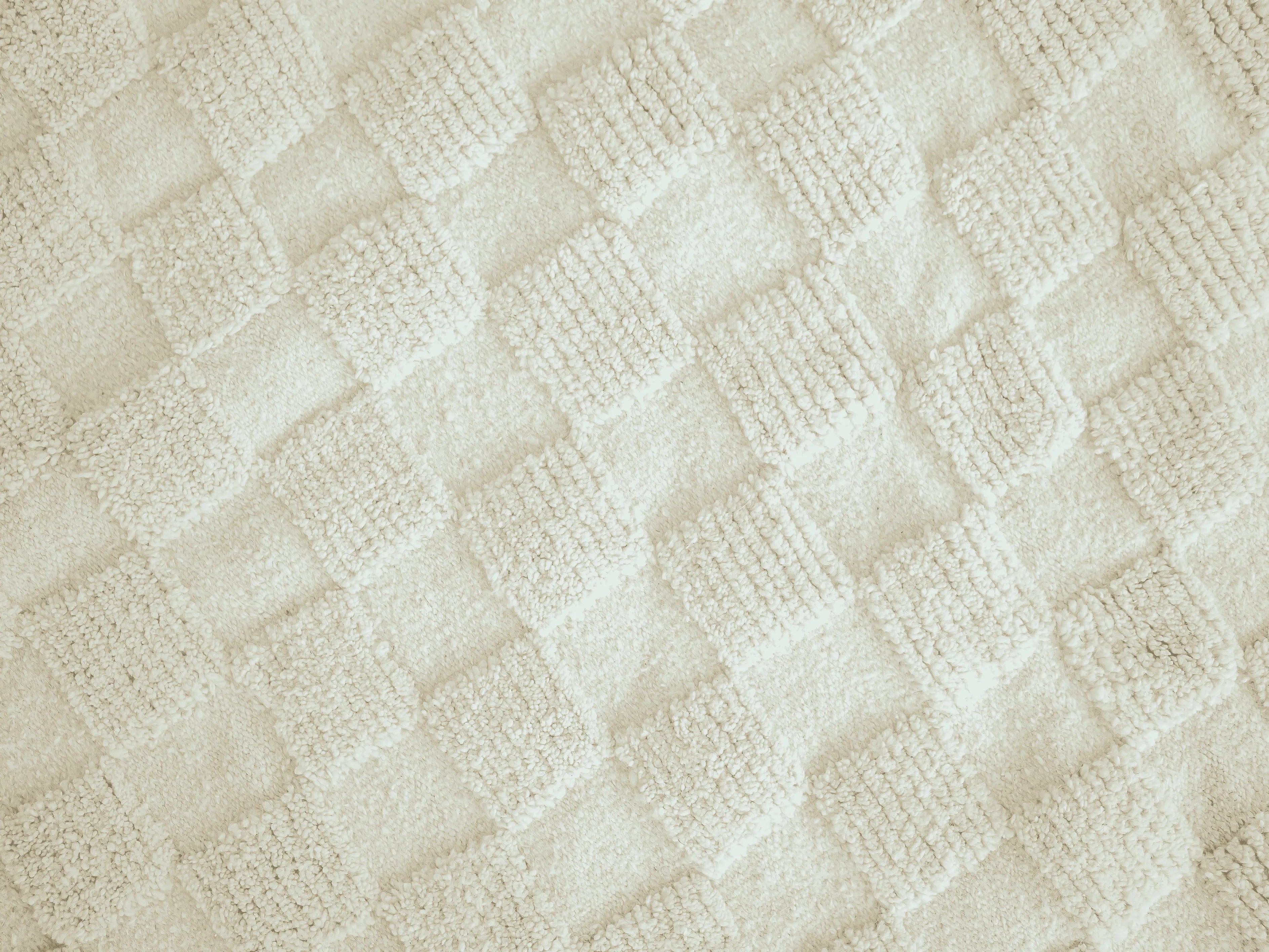 A close up of a natural wool berber rug with repeating ivory geometric squares