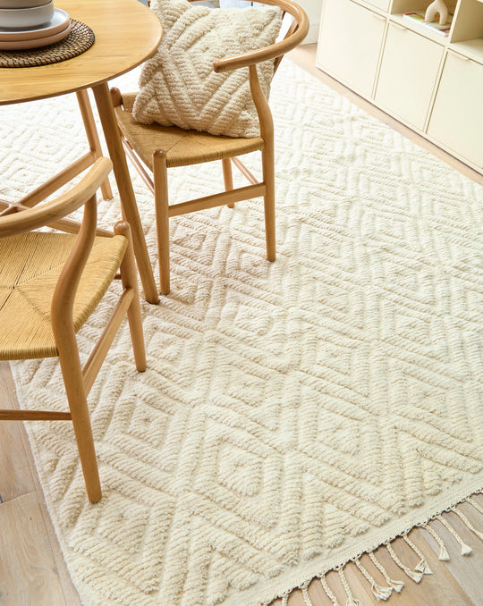 A natural wool cream berber rug with a diamond design on a wooden floor with a wooden table on top.