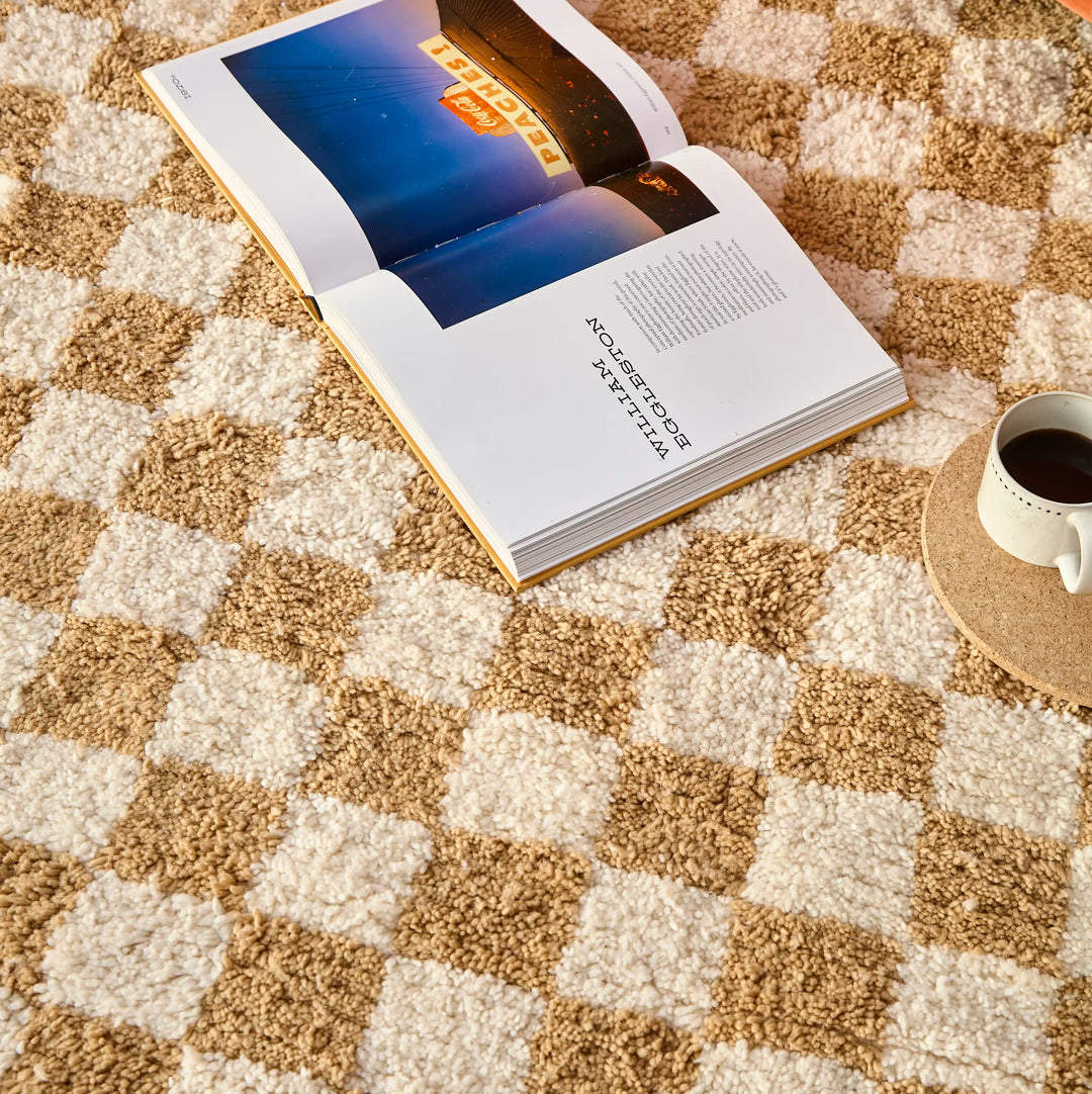 A checkered ochre berber rug with a open photography book on top and a cup of coffee
