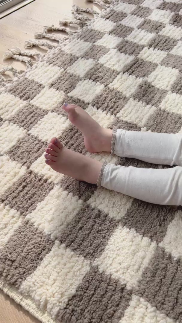 little girl wriggles her toes on a checkered taupe berber wool rug