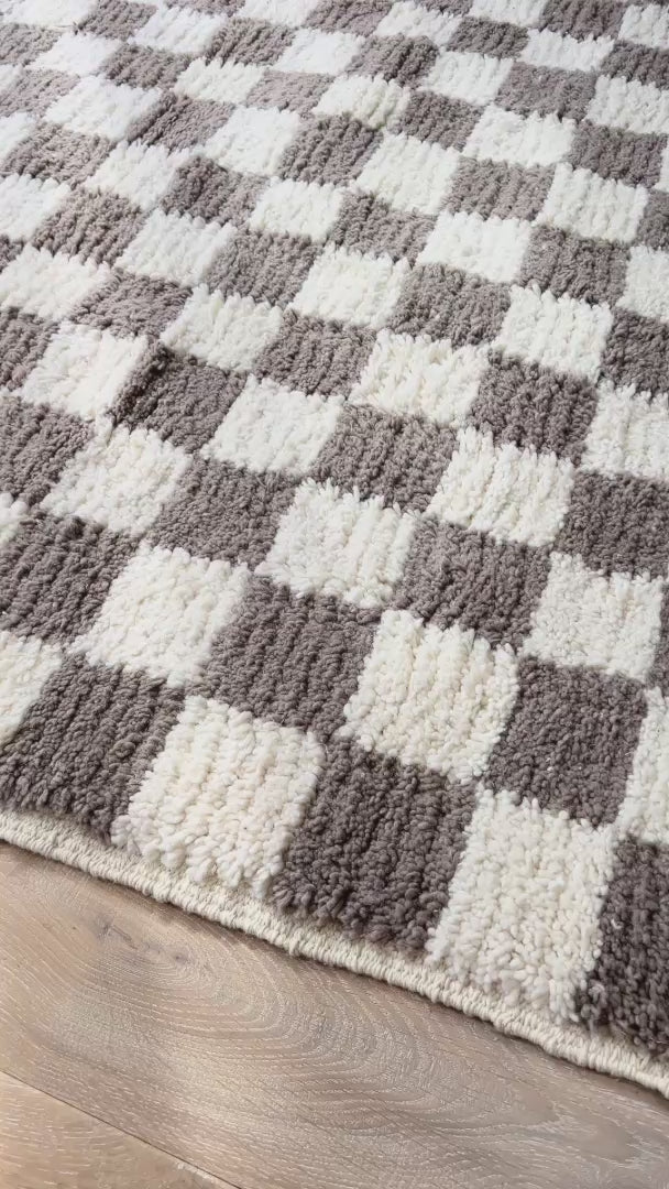 Panning shot of wool checkered taupe berber rug on wooden floor with pink armchair
