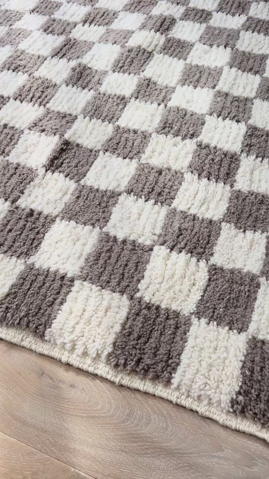 Panning shot of wool checkered taupe berber rug on wooden floor with pink armchair