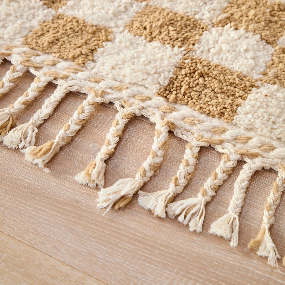 A checkered ochre berber rug with plaited cotton tassels, in a close up