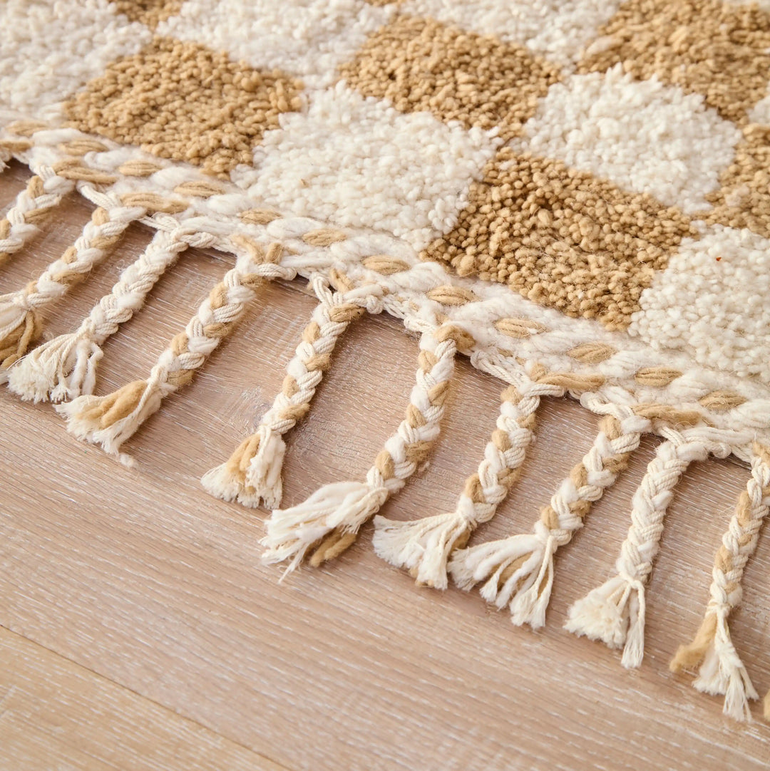 A checkered ochre berber rug with plaited cotton tassels, in a close up